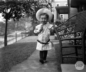 Child Smoking a Pipe in the front yard with a hat