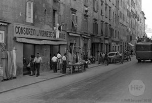 Man Sets Up Shop on Narrow, Bustling Street Beside Apartment Buildings and Pedestrians, Italy 1940s
