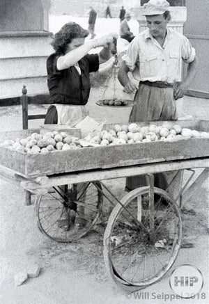 A woman weighs fruit at a vendor's cart in Italy, 1940s.